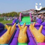 Assault Course Balance Run Outide on grass at corporate fun day at a stadium with crowd and assault course main section in background