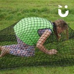Assault Course Scramble Net 2 Hire with a competitor crawling under scramble net on grass in team bib