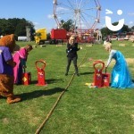 Boom Balloon Blasters Hire at a family fun day with 2 competitors dressed as Anna and Elsa using the balloon blasters with a host compentating and fun bear watchin on