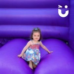 Childrens Turret Bouncy Castle Hire with a toddler smiling at the camera whilst sat on the castle