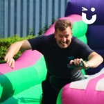 Bungee Run Hire set up at a corporate event zoomed in on a man stretching his arm out with a bean bag to stick to the end of the bungee run