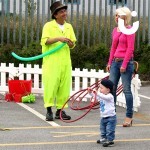 A Clown making a balloon animal whilst a young boy plays with a hoop