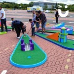 men teaching their children how to play on the crazy golf