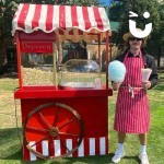 Candy Floss And Popcorn On A Cart 5 Hire set up outside with a fun expert holding a cone of popcorn and a stick of candy floss