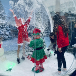 Children dressed in Christmas outfits playing inside the Giant Snow Globe