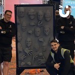 A group of guests pose next to the Life Size Pin Art and the display of many faces they have imprinted on to it at a Corporate Event