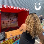 Coconut Shy Stall Hire at a corporate fun day being used by a woman in the sun