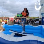 Surf Simulator at a busy corporate promotional fun day with a young woman holding an advertisement