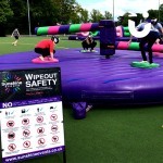 The Wipeout Inflatable Challenge Hire with its safety rules on display as guests take on the challenge of the sweeper arms at a University Event