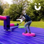 Two guests of a family fun day take on the sweeper arm of the Wipeout Challenge which they have to jump over and duck under