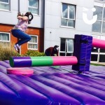 A guest at a University Event takes of 3 others in the wipeout, which sweepers arms spin around trying to take out the challengers