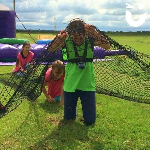 Assault Course Scramble Net 3 Hire with three young girls at a team building event competing and crawling under scramble net wearing bright team bibs